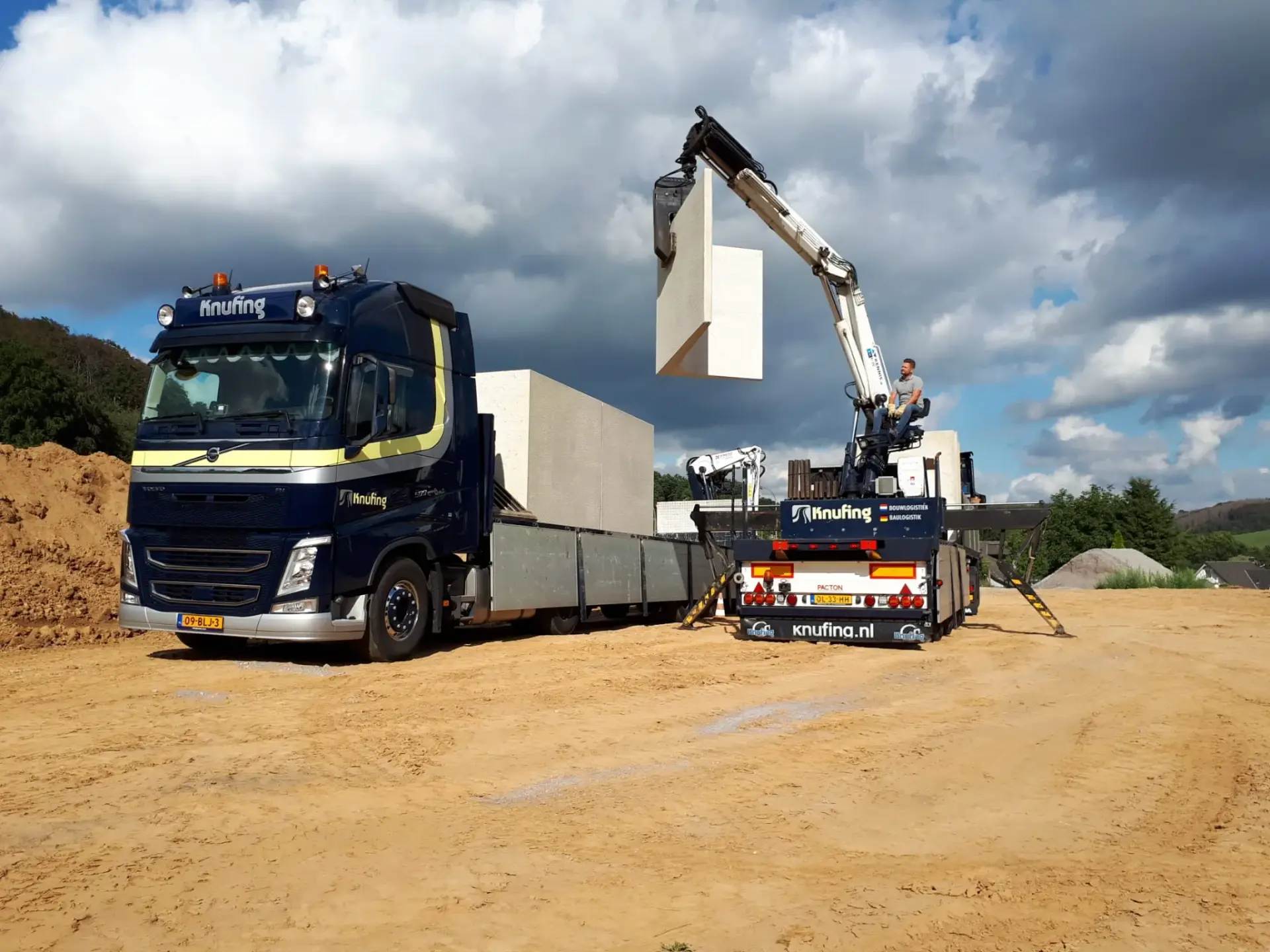 Vrachtwagen met autolaadkraan die zelfstandig een betonwand lost op locatie